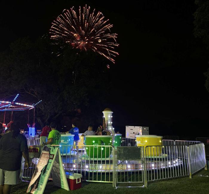 Teacup ride setup at night with fireworks in the background